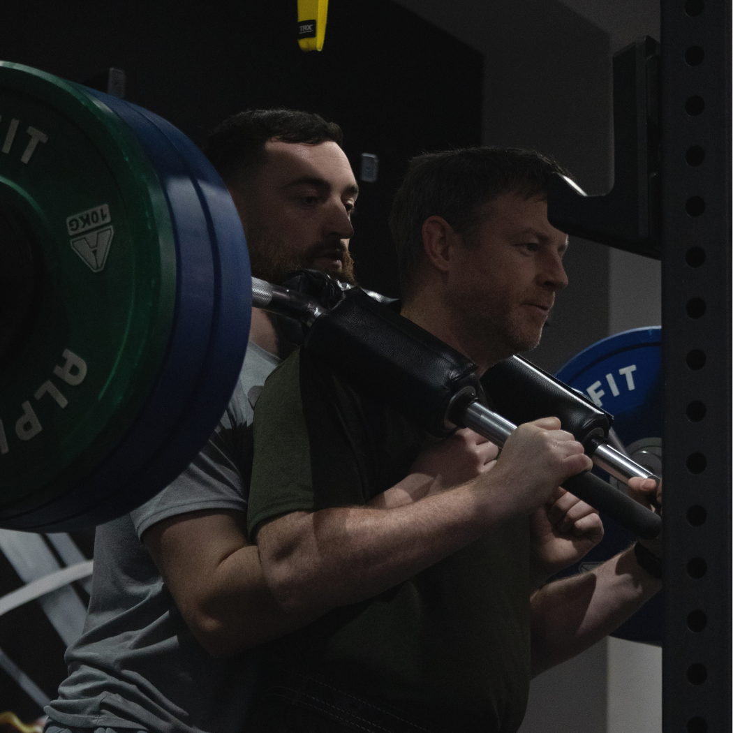 Coach Dermo spotting a client during a barbell squat